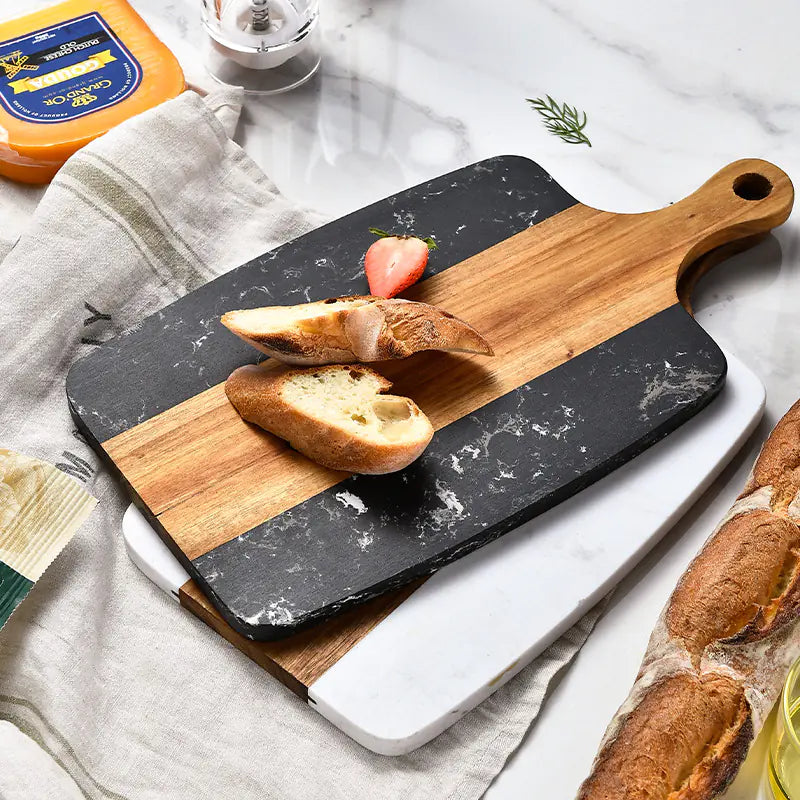 Two-tiered cutting board with marble base and wooden top, displaying bread slices and a strawberry.