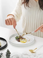 Person eating a dish with a fork and knife on a marble-patterned plate.