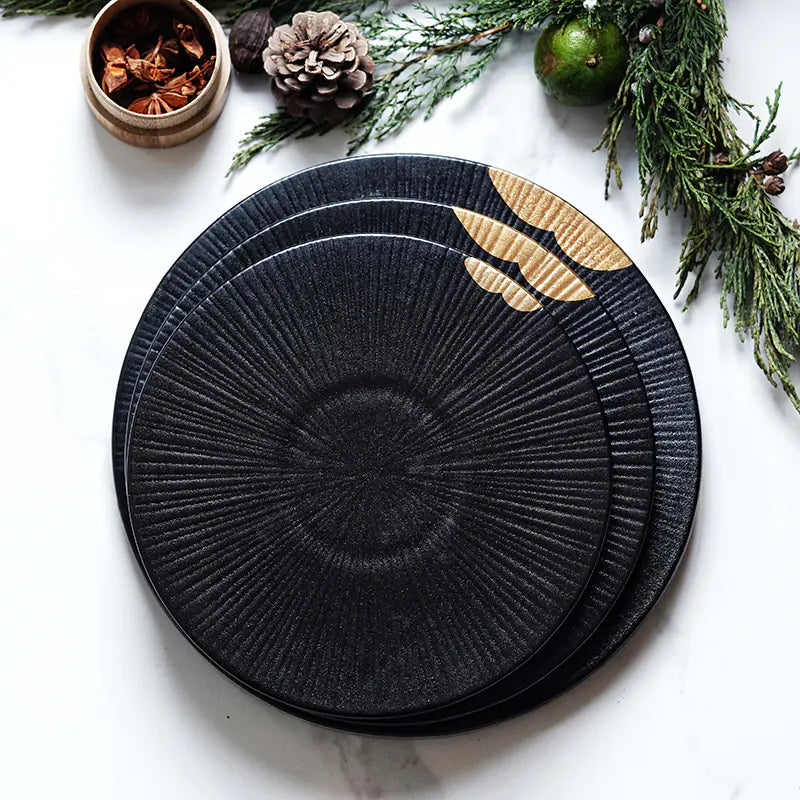 Black textured plates with gold leaf design on a white surface with decorative elements.