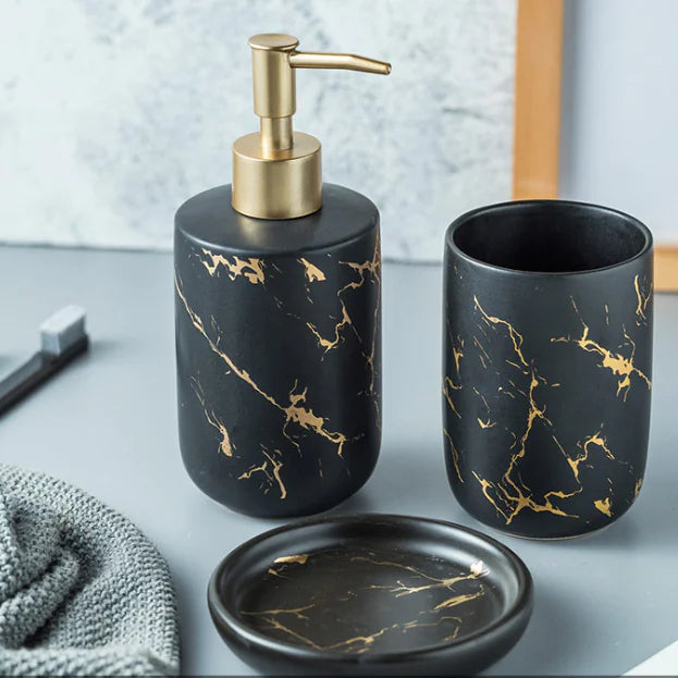 Black and gold marbled bathroom set with dispenser, cup, and soap dish on a light gray surface.