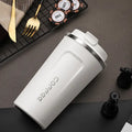 White travel mug with silver lid on a dark surface with gaming items.