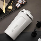 White travel mug with silver lid on a dark surface with gaming items.