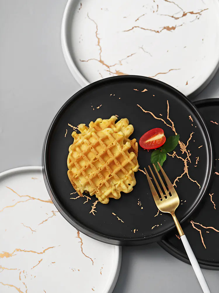 Black plate with waffle, tomato, and mint leaf on a marble surface