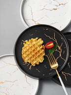 Black plate with waffle, tomato, and mint leaf on a marble surface