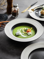Green soup in a white bowl with garnishes on a dark surface