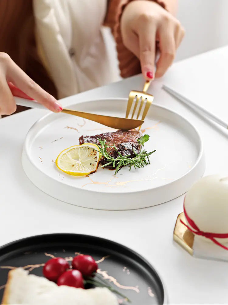Person cutting into a piece of meat on a white plate with lemon and rosemary, with a blurred background.
