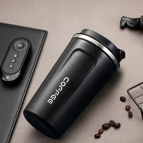 Black travel mug with 'Corffe' branding on a beige surface with coffee beans and a remote control.